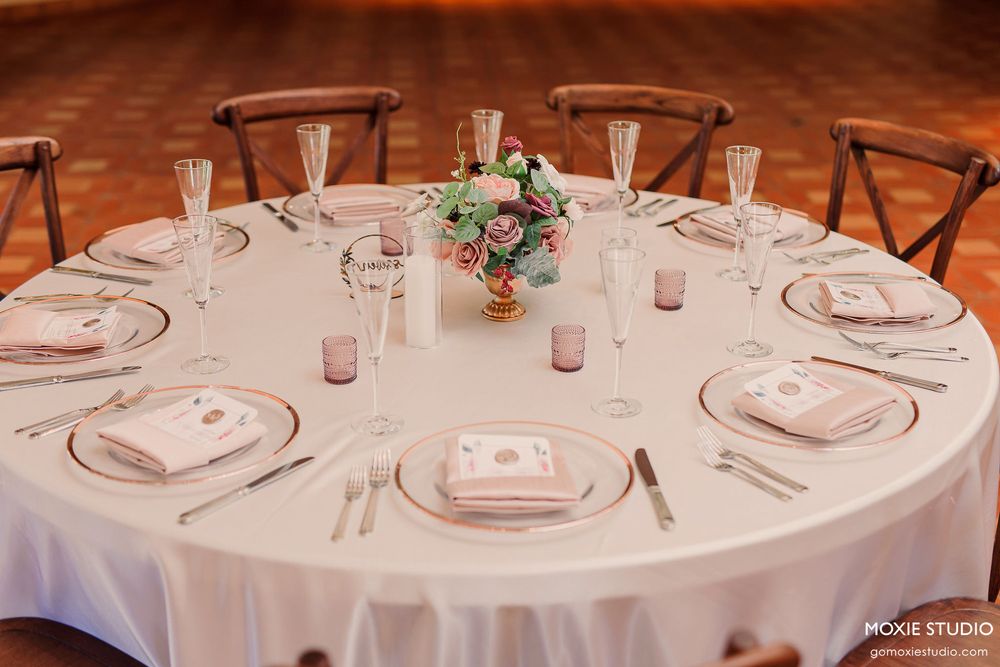 Elegant wedding reception table setting with white linens, pink glassware, and a floral centerpiece.