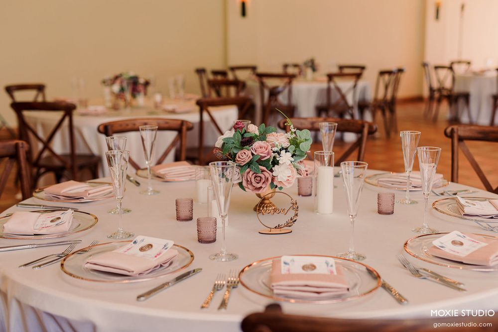 Elegant wedding reception tables set with pink glassware, white plates, and floral centerpieces in a rustic venue.