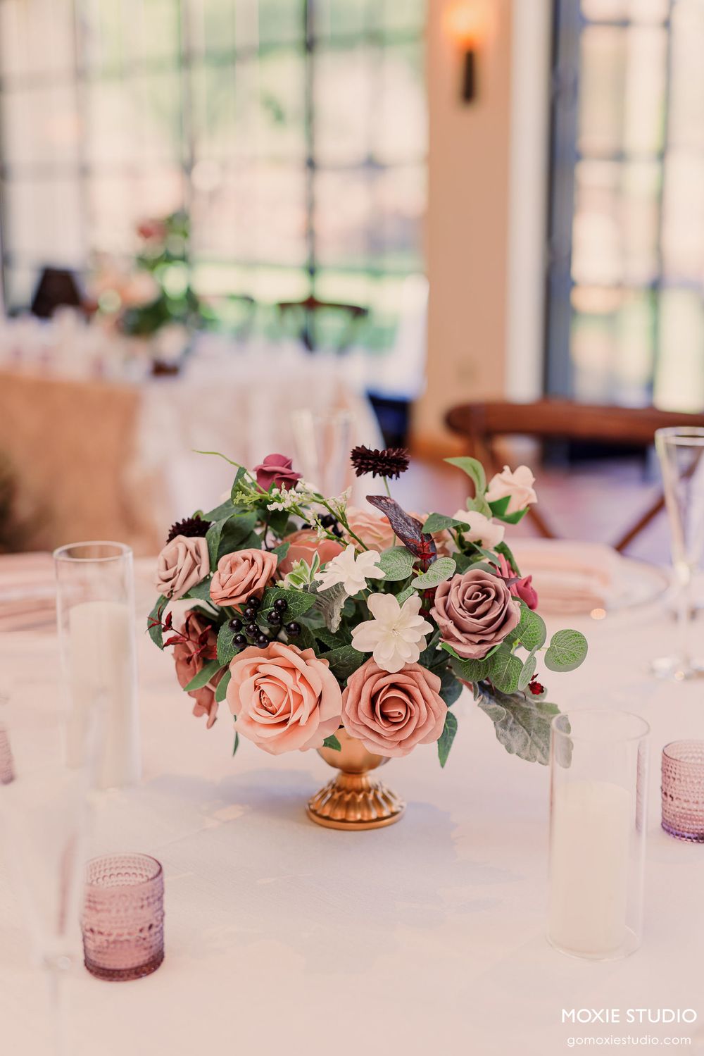 Elegant wedding table decor with pink and mauve roses in gold vases and pink tinted glass votives.