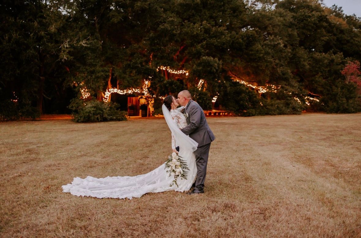 Sunset wedding portrait with bride's train flowing in grassy field.