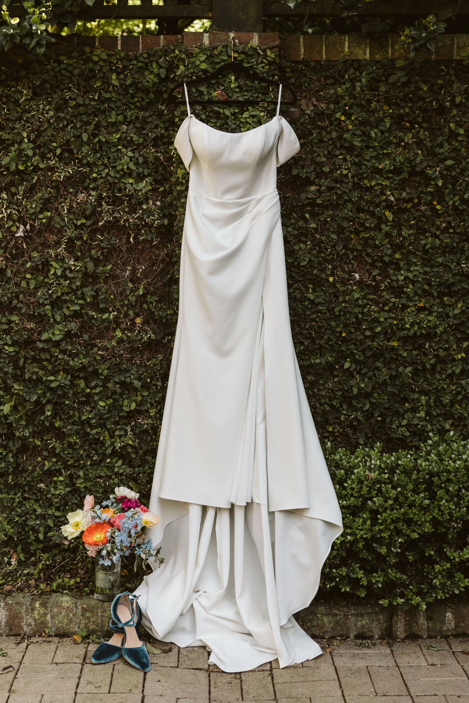 Elegant white wedding dress displayed against lush green hedge backdrop.