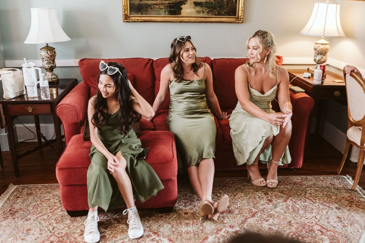 Wedding party relaxing on red couches during pre-ceremony preparations.