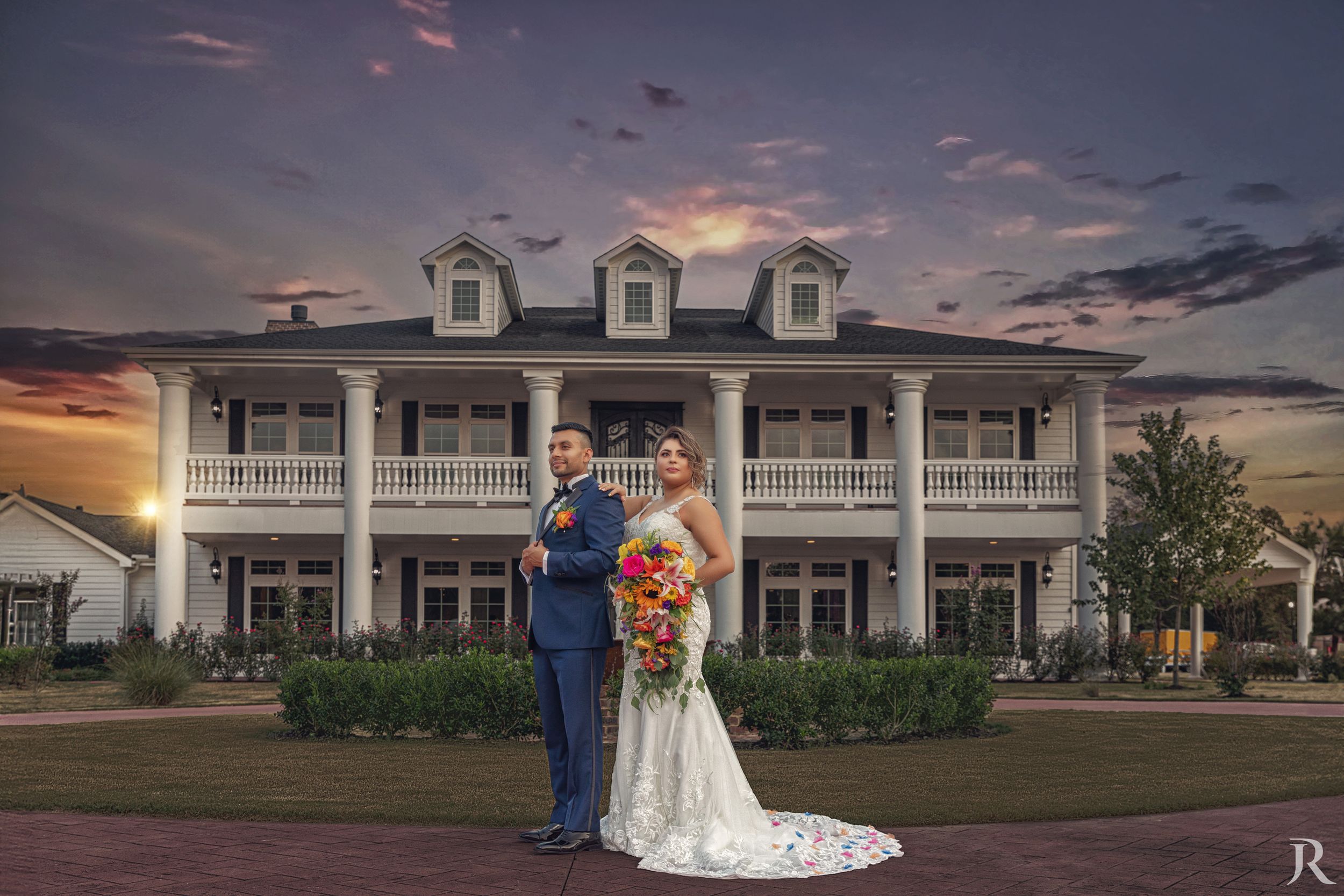 Bride and groom in front of a white mansion at sunset