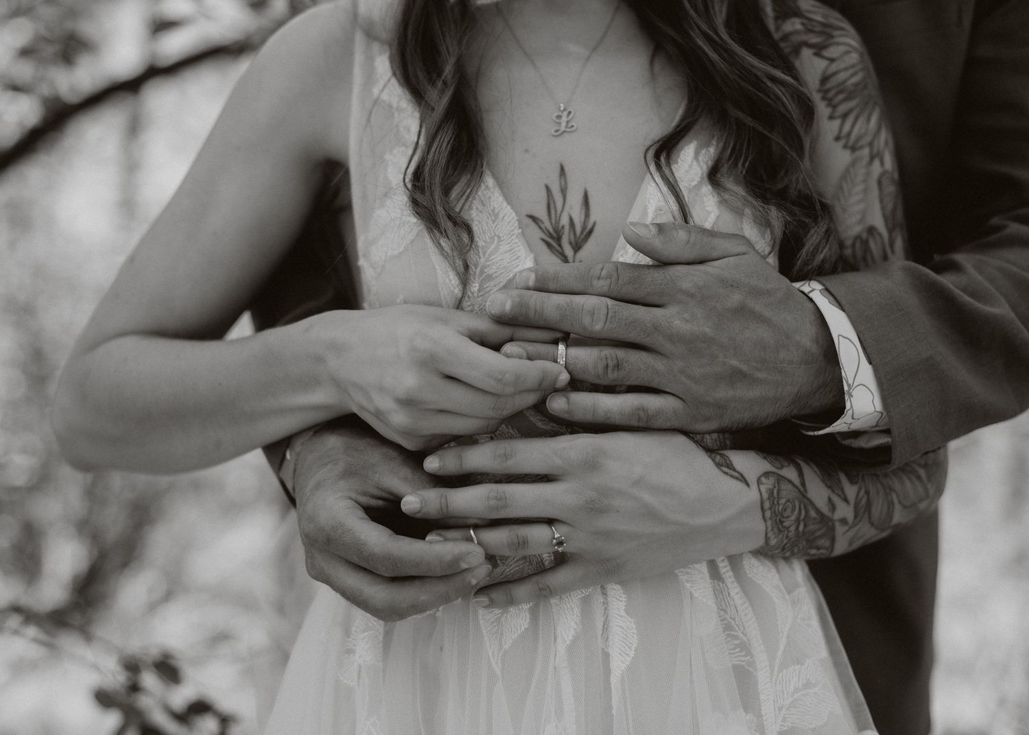 Detailed black and white closeup of hands with tattoos placing a wedding ring in intimate bride and groom moment.