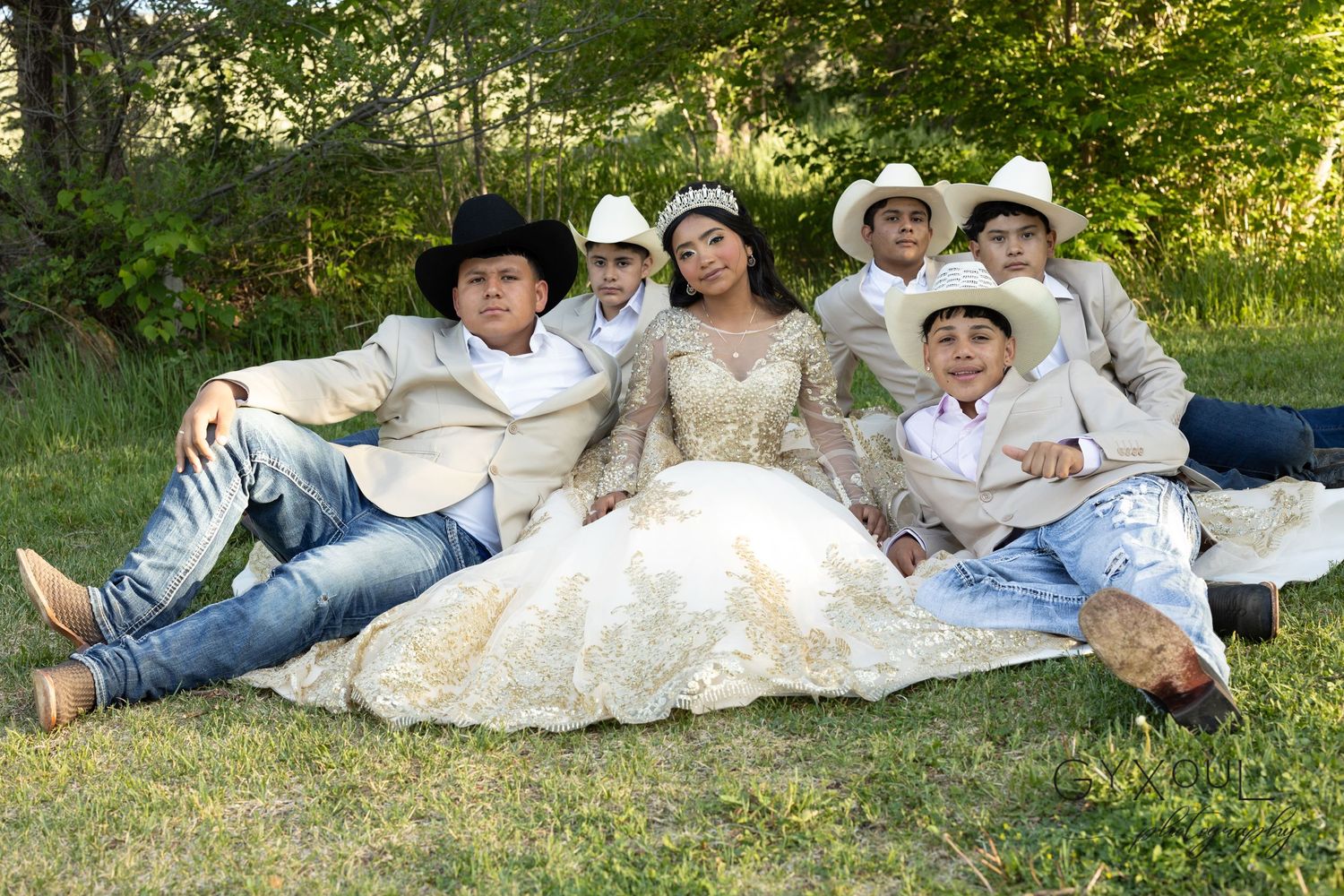 A quinceañera group photo on grass with guests in white western attire relaxing together.