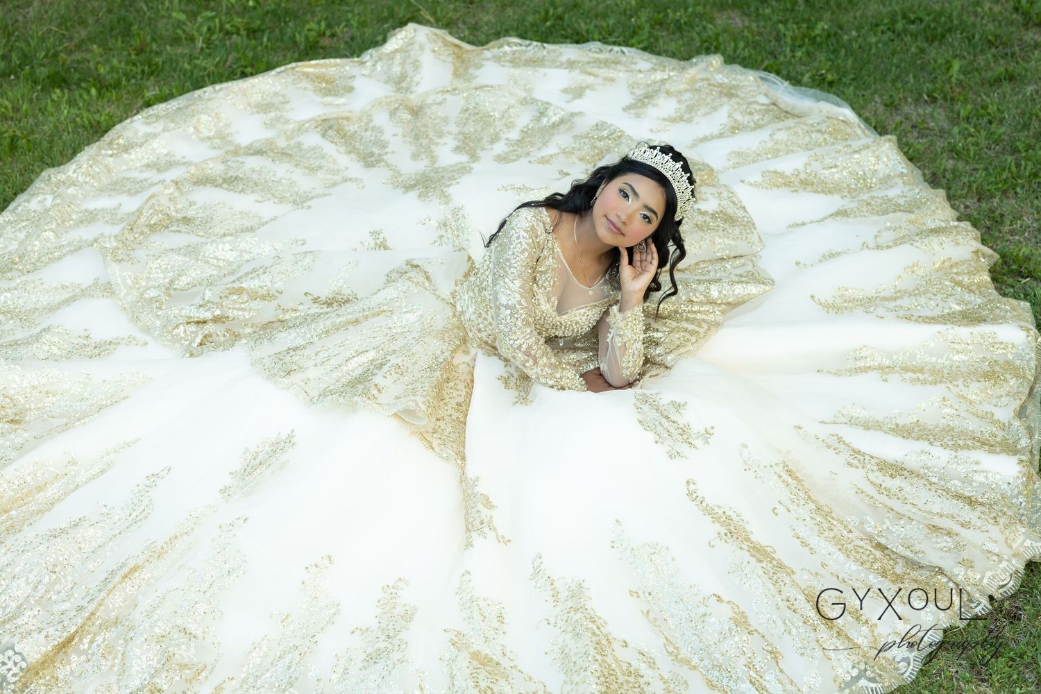 An overhead view of an elaborate cream ballgown with intricate lace details spread out on green grass.