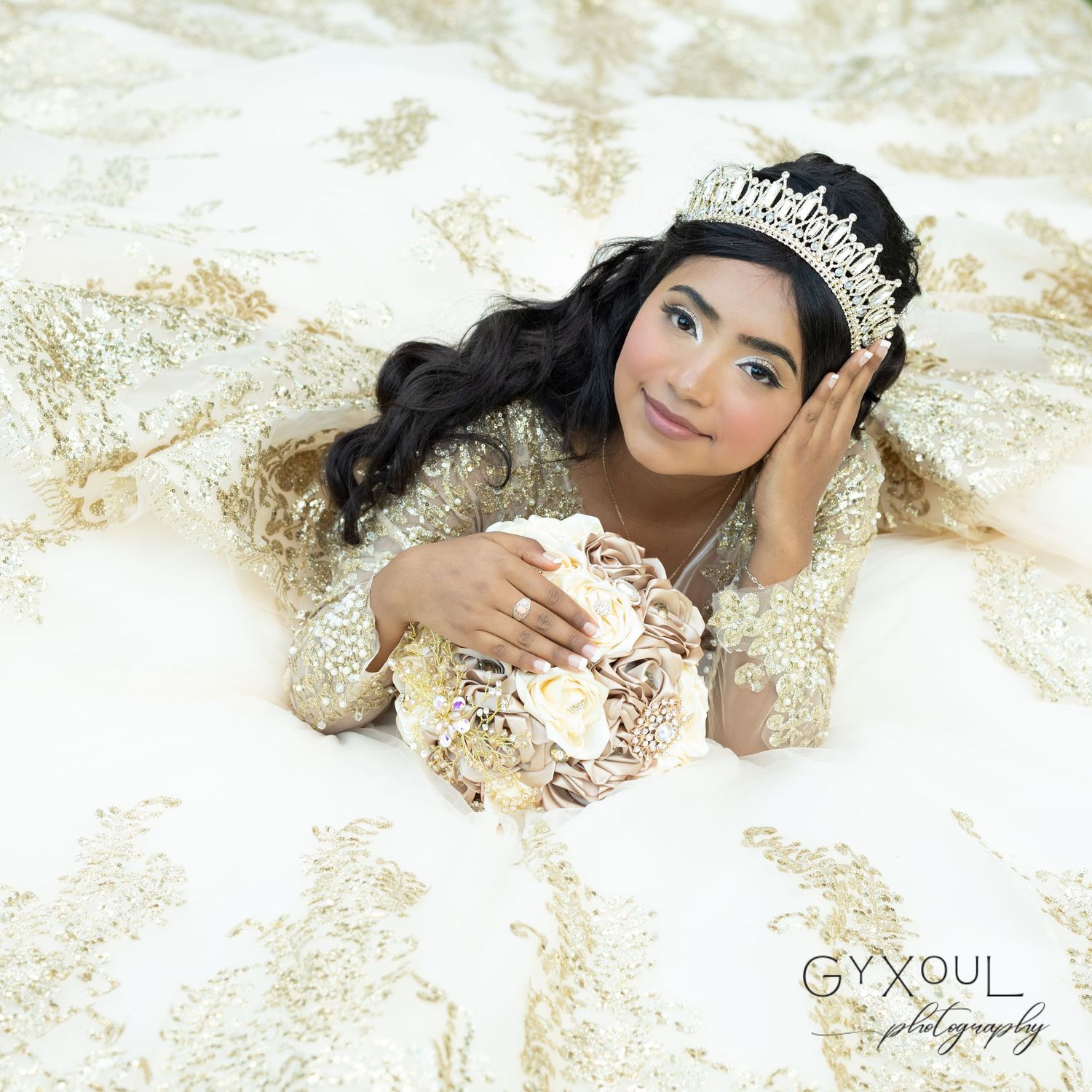 A stunning cream-colored quinceañera gown with intricate beading and a sparkling tiara photographed against a light backdrop.