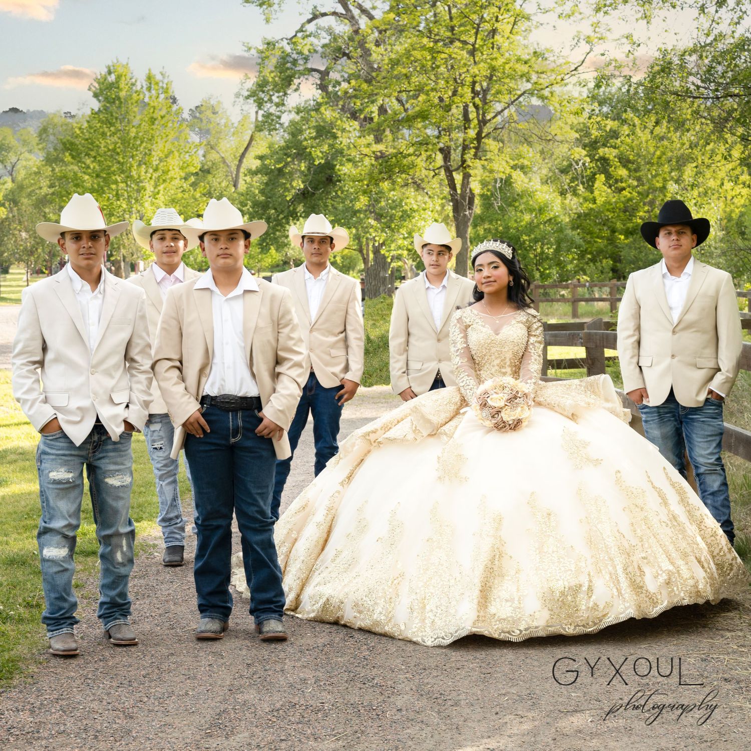 A wedding party poses outdoors wearing white jackets and cowboy hats against a scenic countryside backdrop.