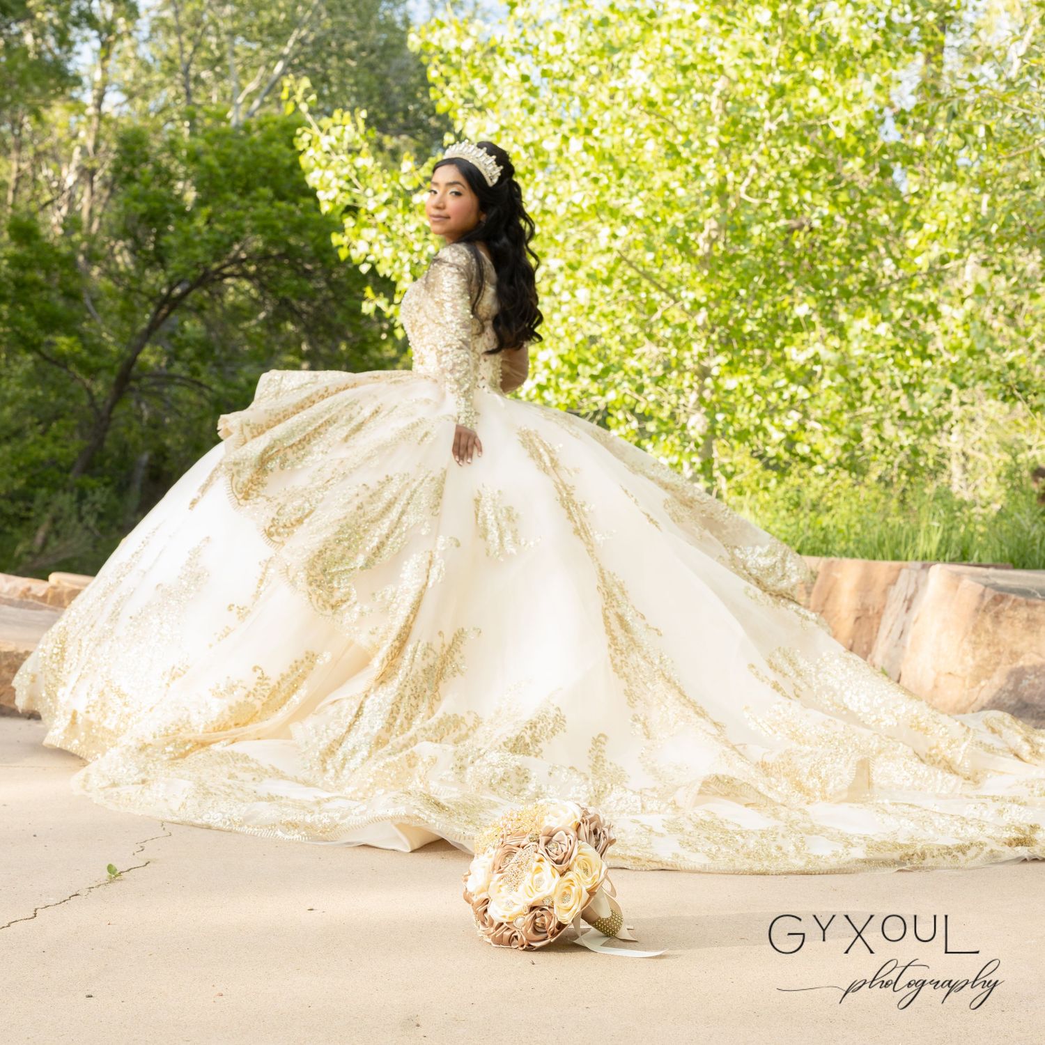 A dramatic full-length shot of a luxurious cream ballgown with a flowing train amidst green foliage.