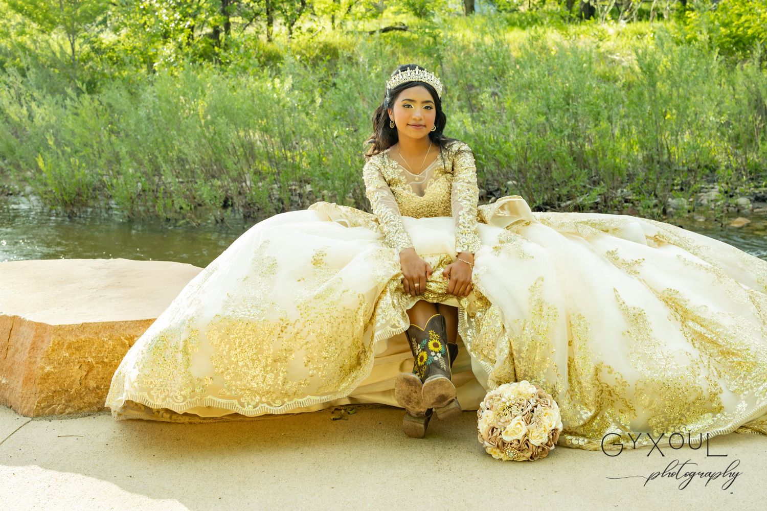 A serene outdoor portrait featuring an ornate cream-colored ballgown and bouquet near a waterside setting.
