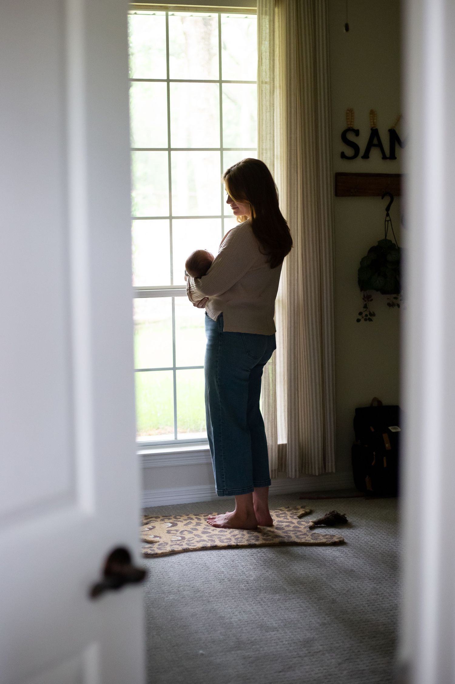A silhouette stands by a bright window holding a baby in a peaceful moment.