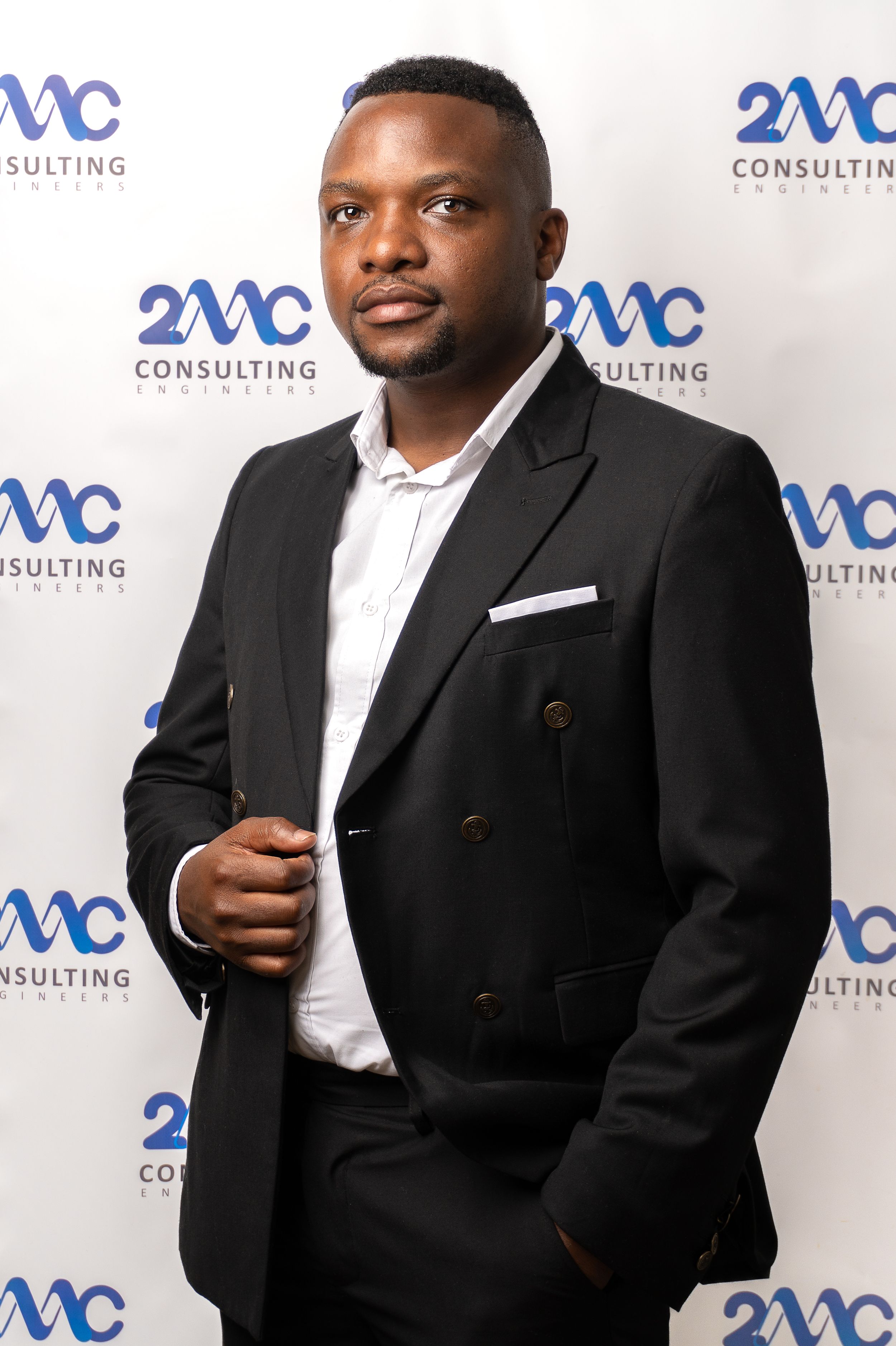 Professional business portrait against corporate backdrop wearing black suit and white shirt.