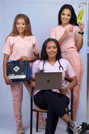 Healthcare professionals in pink scrubs posing with medical equipment and laptop.