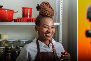 Cheerful chef wearing brown apron and hair wrap in commercial kitchen with red cookware.