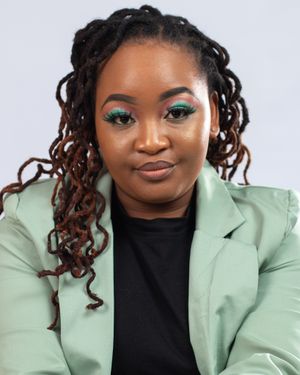 Professional portrait of a woman in mint blazer with long brown locs and vibrant teal eyeshadow against light background.