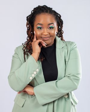 Woman in sage green blazer poses with hand on cheek while wearing dramatic teal eye makeup.