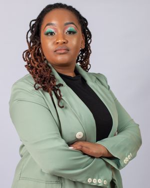 Professional wearing mint green blazer and black top strikes confident pose with arms crossed.