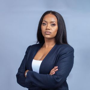 Professional headshot of a businesswoman against a blue background wearing a navy blazer.