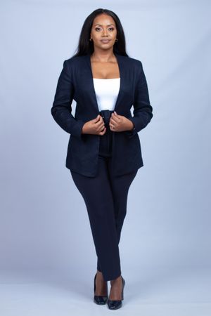 Professional woman in navy business suit and white top posing against grey background.