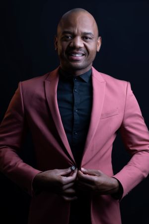 Professional portrait against dark background featuring person in salmon pink blazer and black shirt.