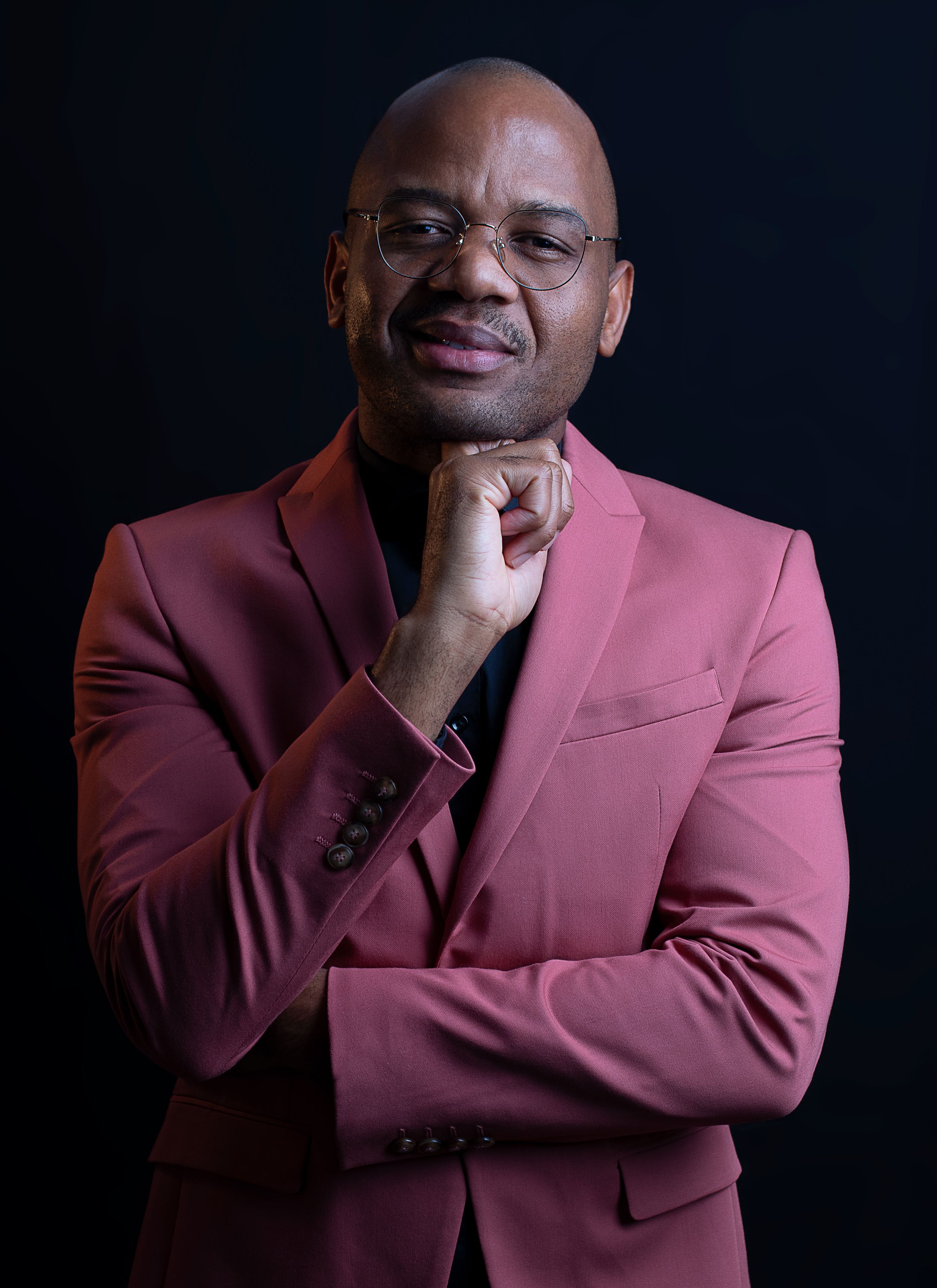 Professional portrait against dark background showing contemplative pose in burgundy suit jacket.