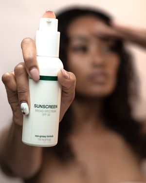 Hand holding up a white bottle of sunscreen against a blurred background.