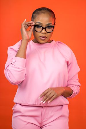 Stylish portrait against an orange background featuring pink athleisure wear and cat-eye glasses.