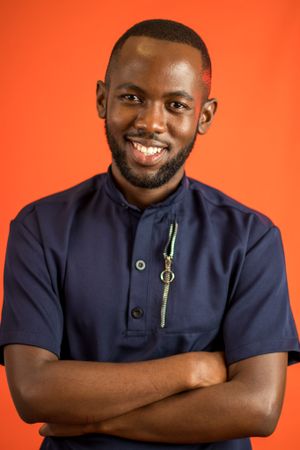 Portrait in navy blue shirt against vibrant orange background.