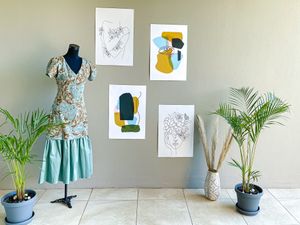 A floral dress on a mannequin with artwork and potted plants displayed against a beige wall.