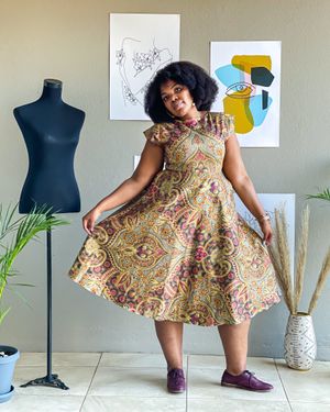 A vintage-style paisley print dress styled with purple shoes in a studio with abstract wall art.