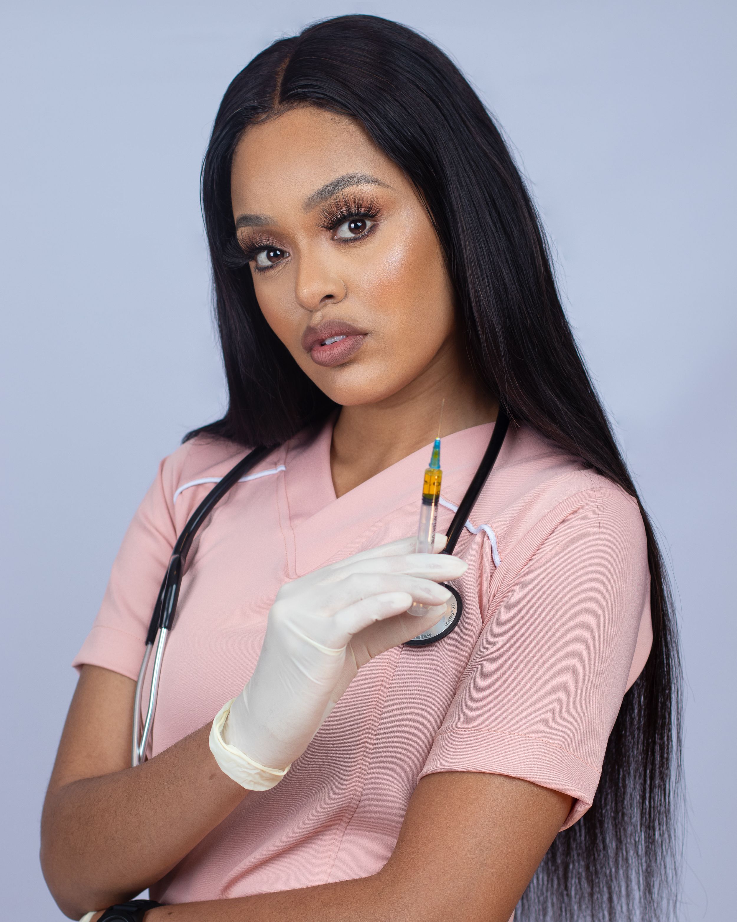 Healthcare worker in pink scrubs holding syringe against blue background.