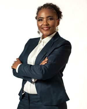 Professional business portrait with arms crossed wearing navy suit against white background.