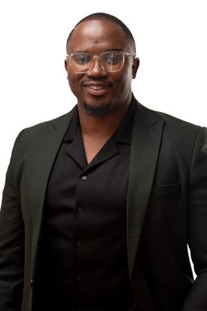Professional studio portrait of person wearing glasses, dark blazer and button-down shirt.