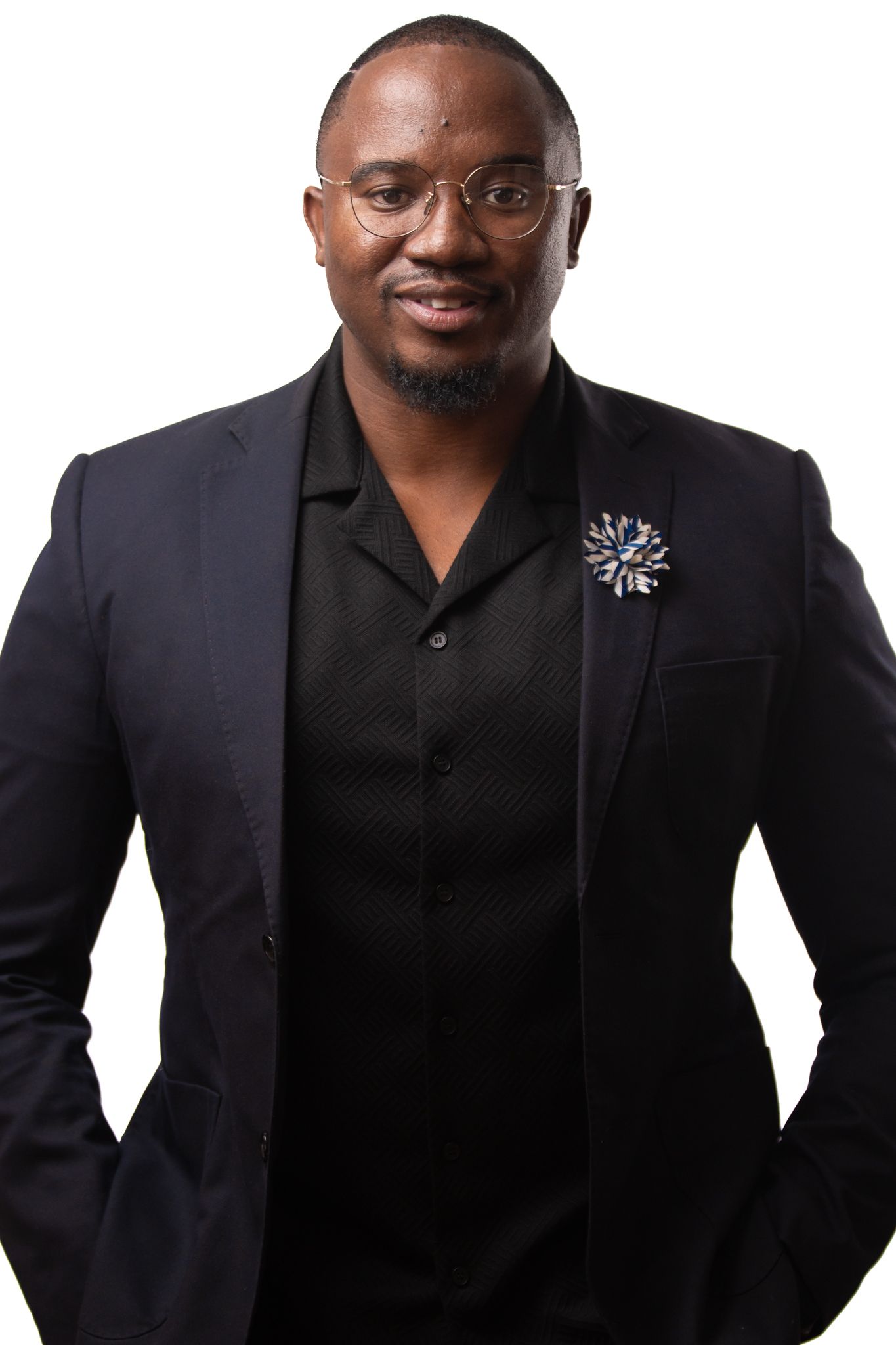 Professional portrait of someone wearing a black blazer with decorative brooch pin and black shirt against white background.