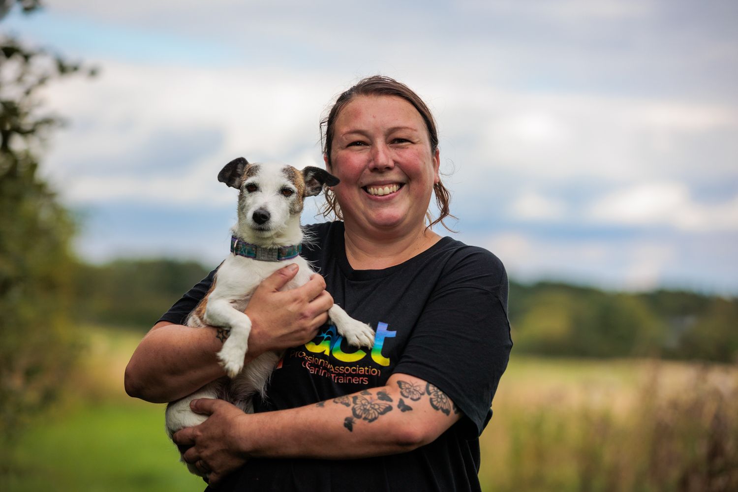 A joyful moment outdoors with a small Jack Russell terrier wearing a colorful outfit being held in someone's arms.
