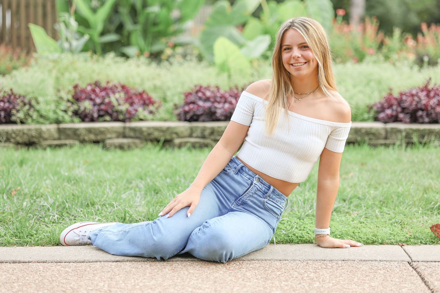 Casual outdoor portrait of someone in blue jeans and white crop top sitting on concrete.
