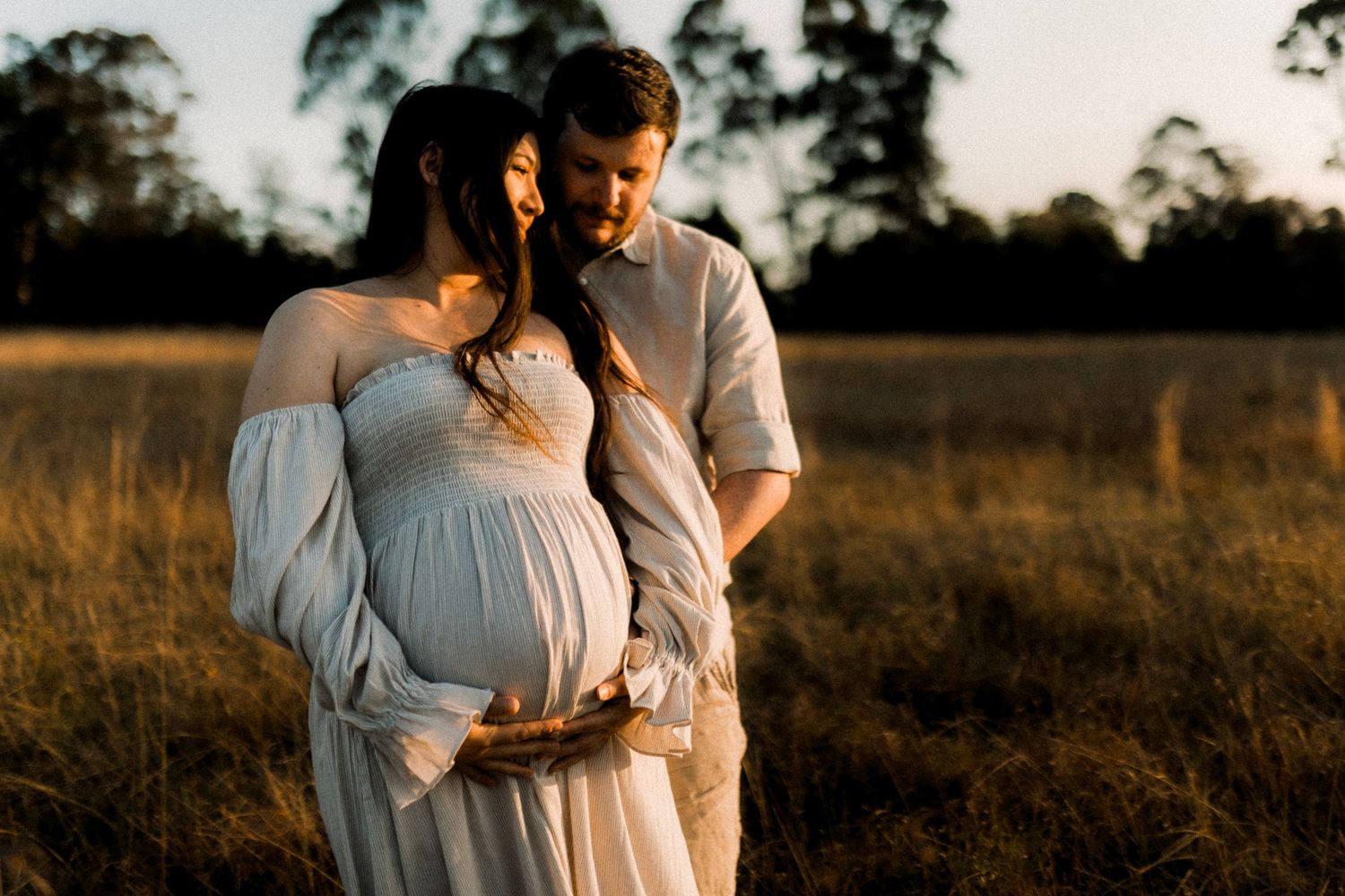 Couple embracing in a golden field at sunset during maternity photo session.