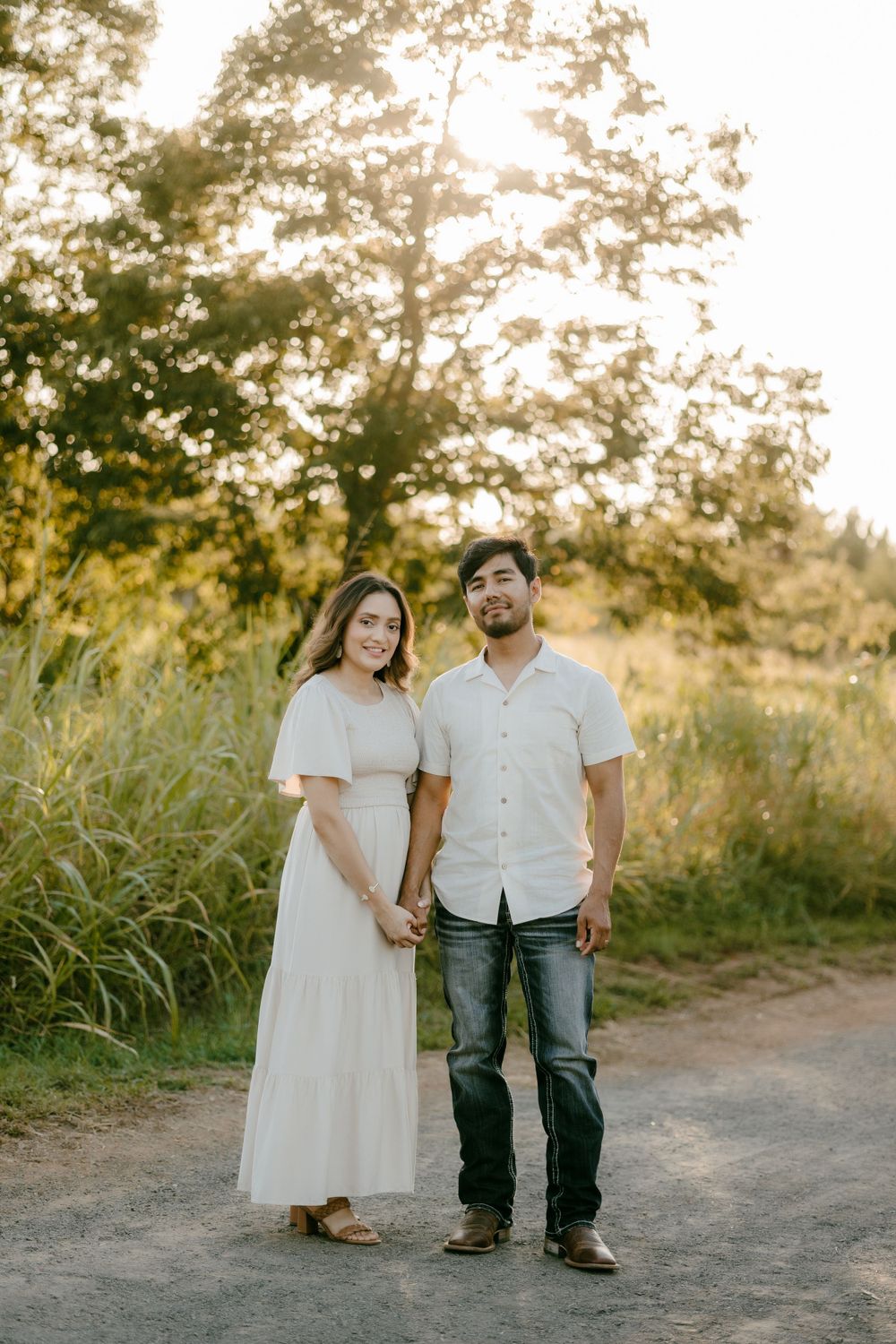 Couple standing together on dirt path during golden hour sunset.
