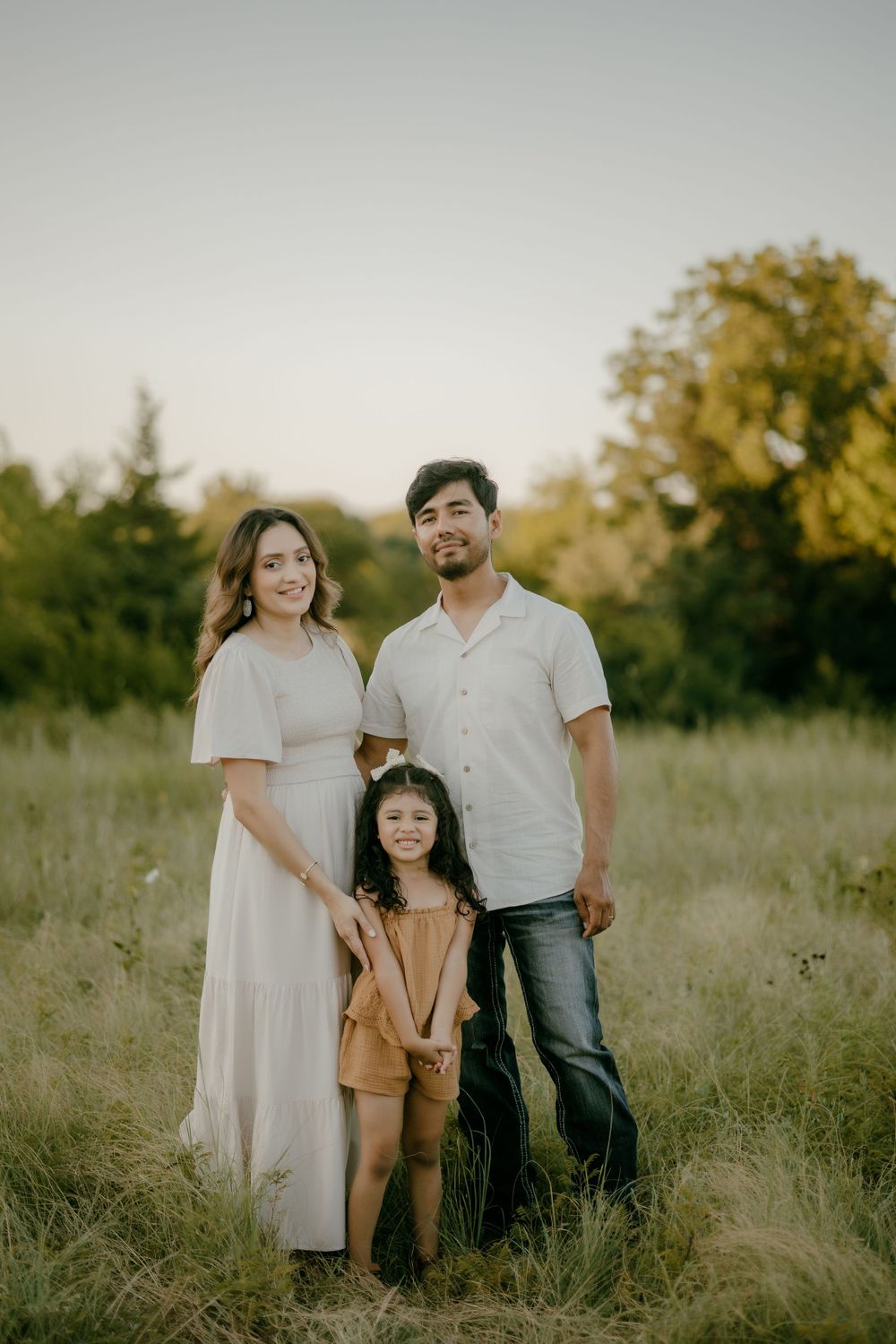 Family of three poses together in a rustic field during golden hour photography session.