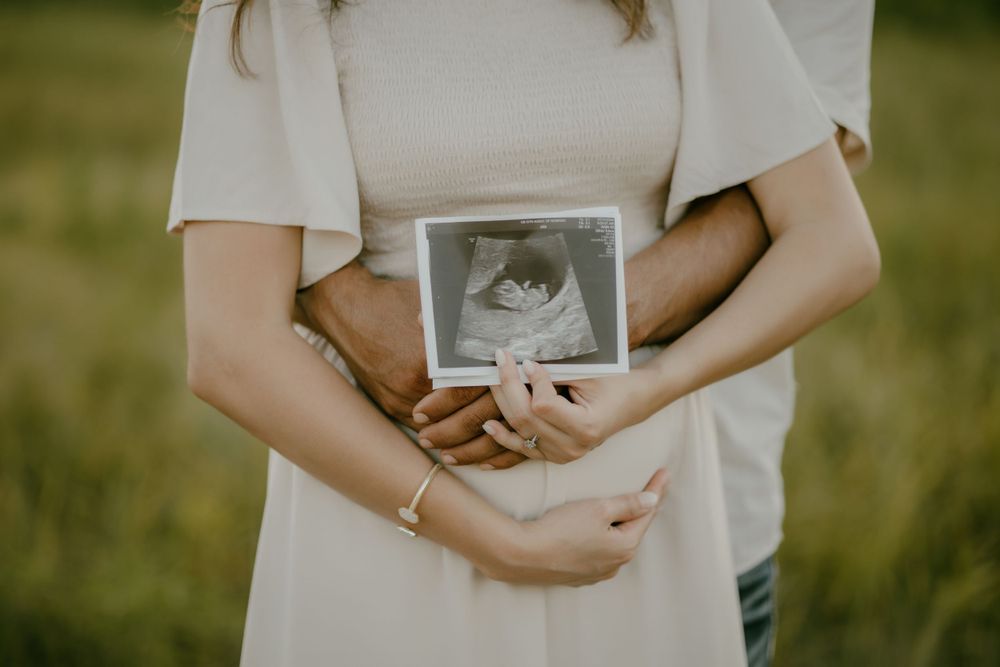 Close-up of hands holding ultrasound photos against white dress.