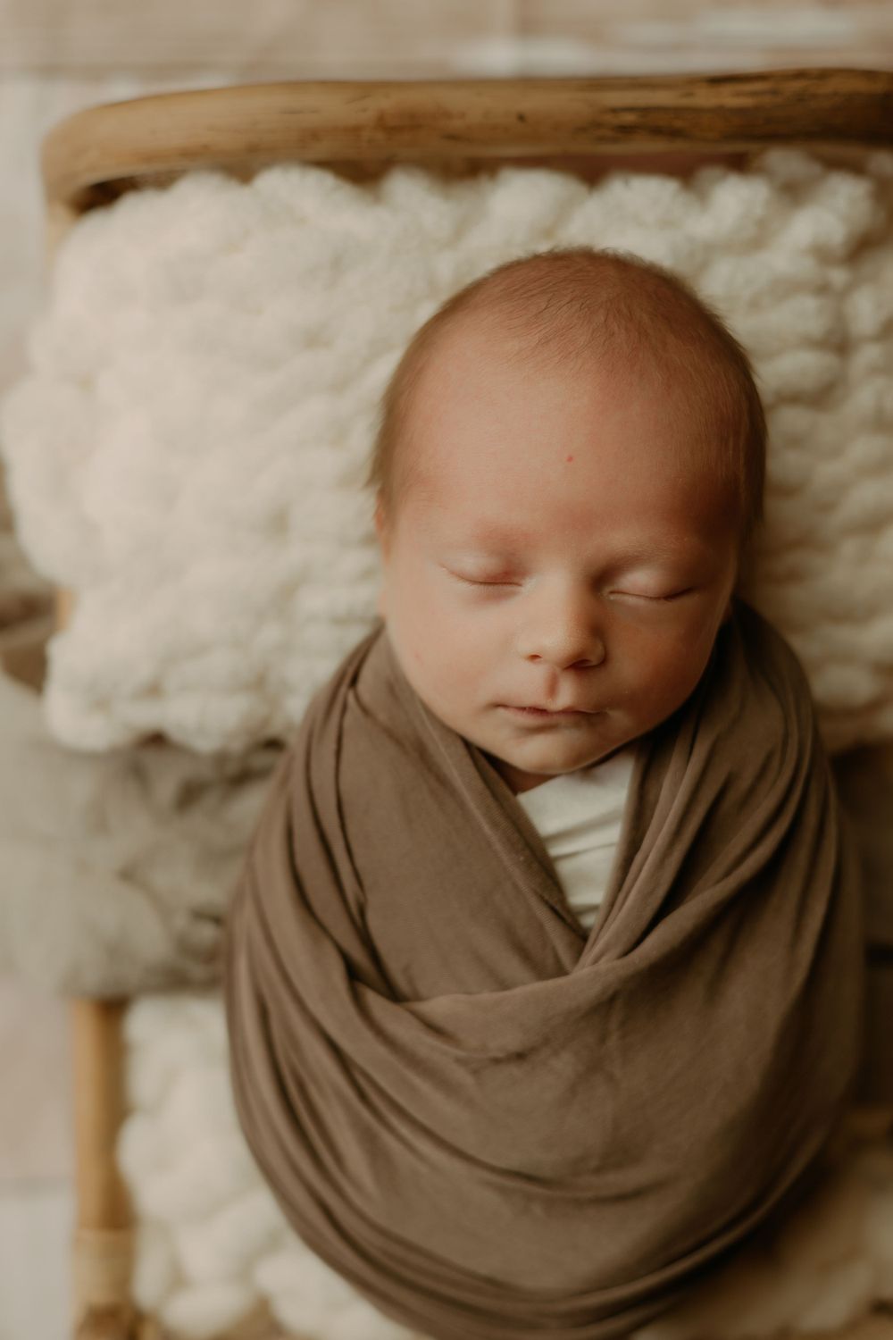 Peaceful newborn swaddled in brown fabric against neutral backdrop.