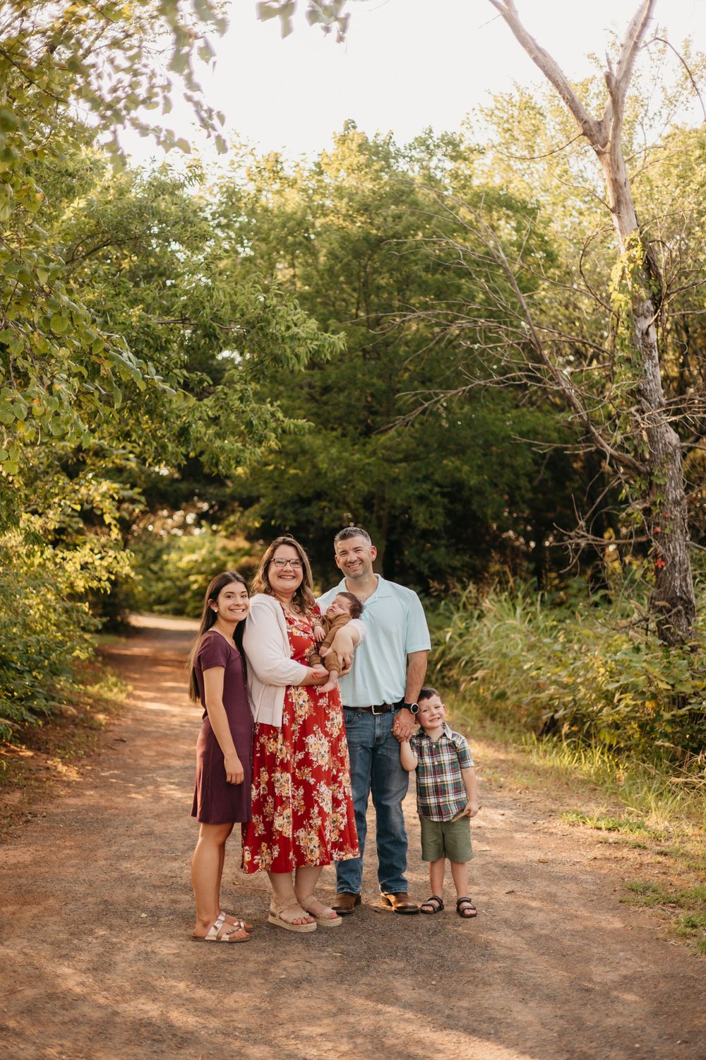 A family of five poses together on a tree-lined dirt path during golden hour.