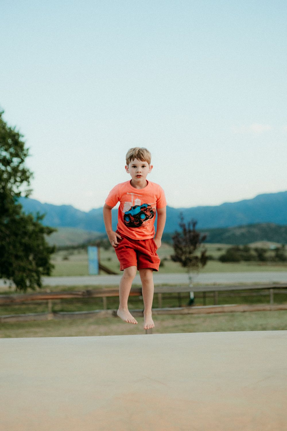 Three sequential photos show a child in an orange shirt jumping on an outdoor surface with mountains in the background.