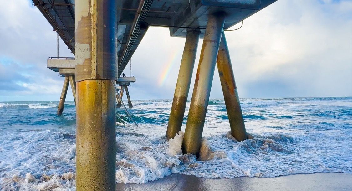 Ocean waves crashing against wooden pier supports during high tide.
