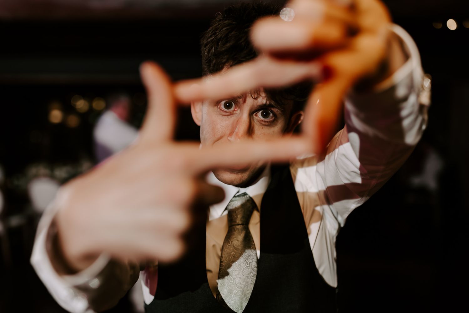 Creative framing shot of someone wearing a suit and tie making a finger frame gesture in moody lighting.