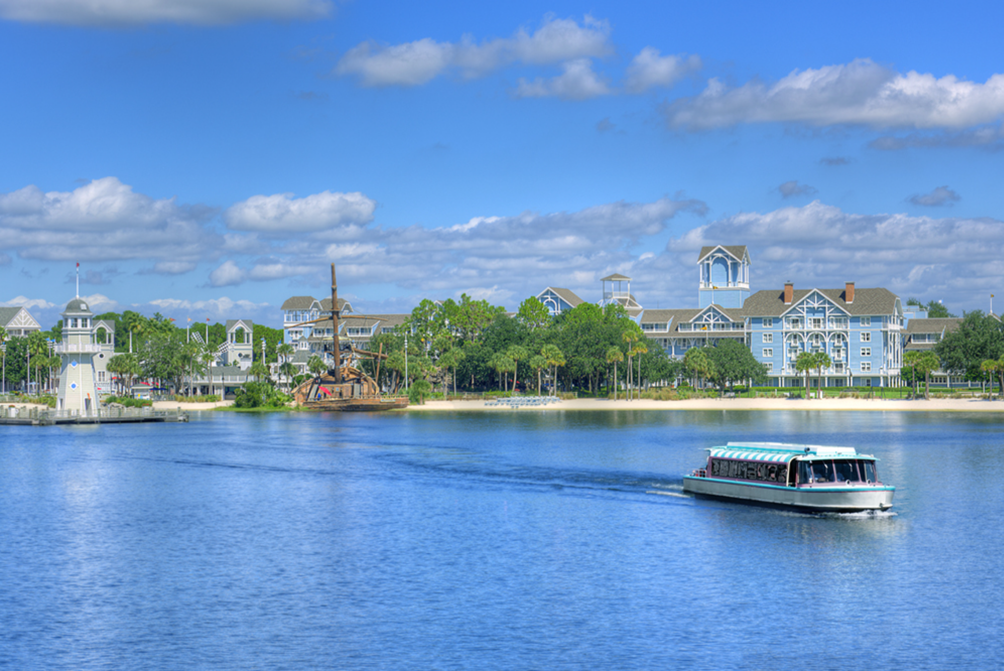 Tranquil waterfront view of resort buildings and boat on calm blue waters.