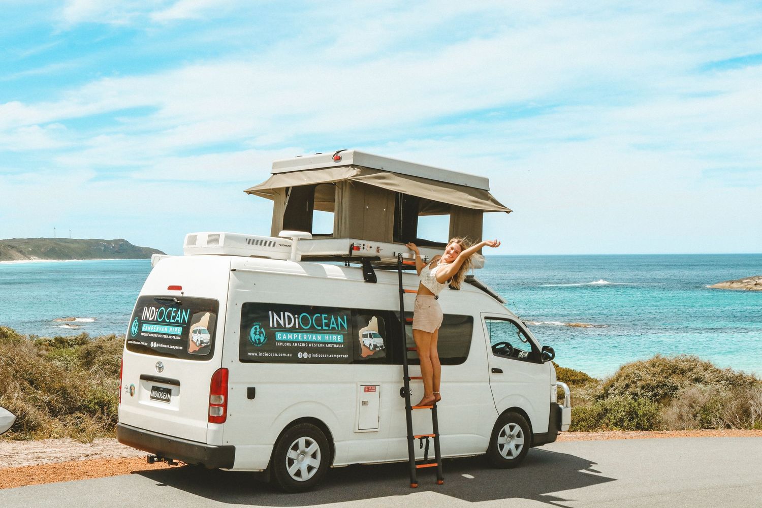 White camper van with pop-up roof parked along coastal highway with turquoise ocean views.