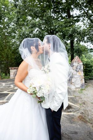 A romantic wedding couple share a kiss under a flowing white veil in an outdoor garden setting with stone features. NJ wedding photographer