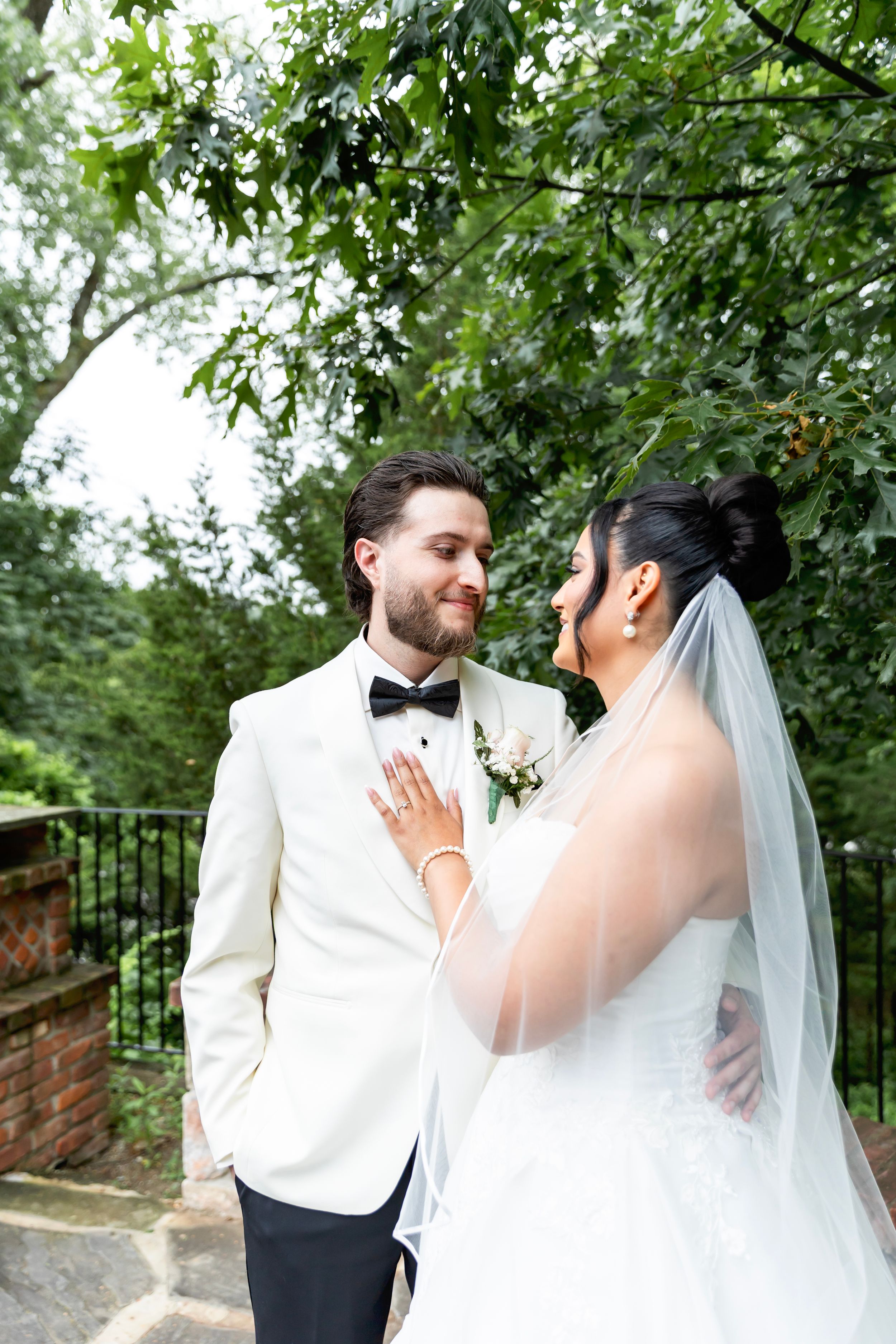 A wedding couple shares an intimate moment outdoors among green trees and brick walls. NJ wedding photographer | Sarah Jane Photography LLC