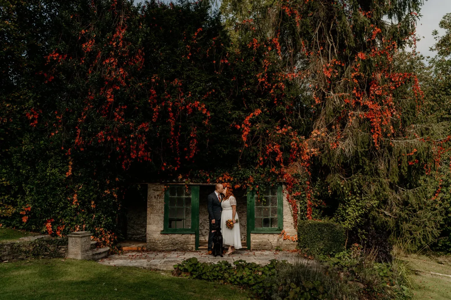 A romantic outdoor wedding ceremony setup with wooden chairs surrounded by autumn trees and red fall foliage.
